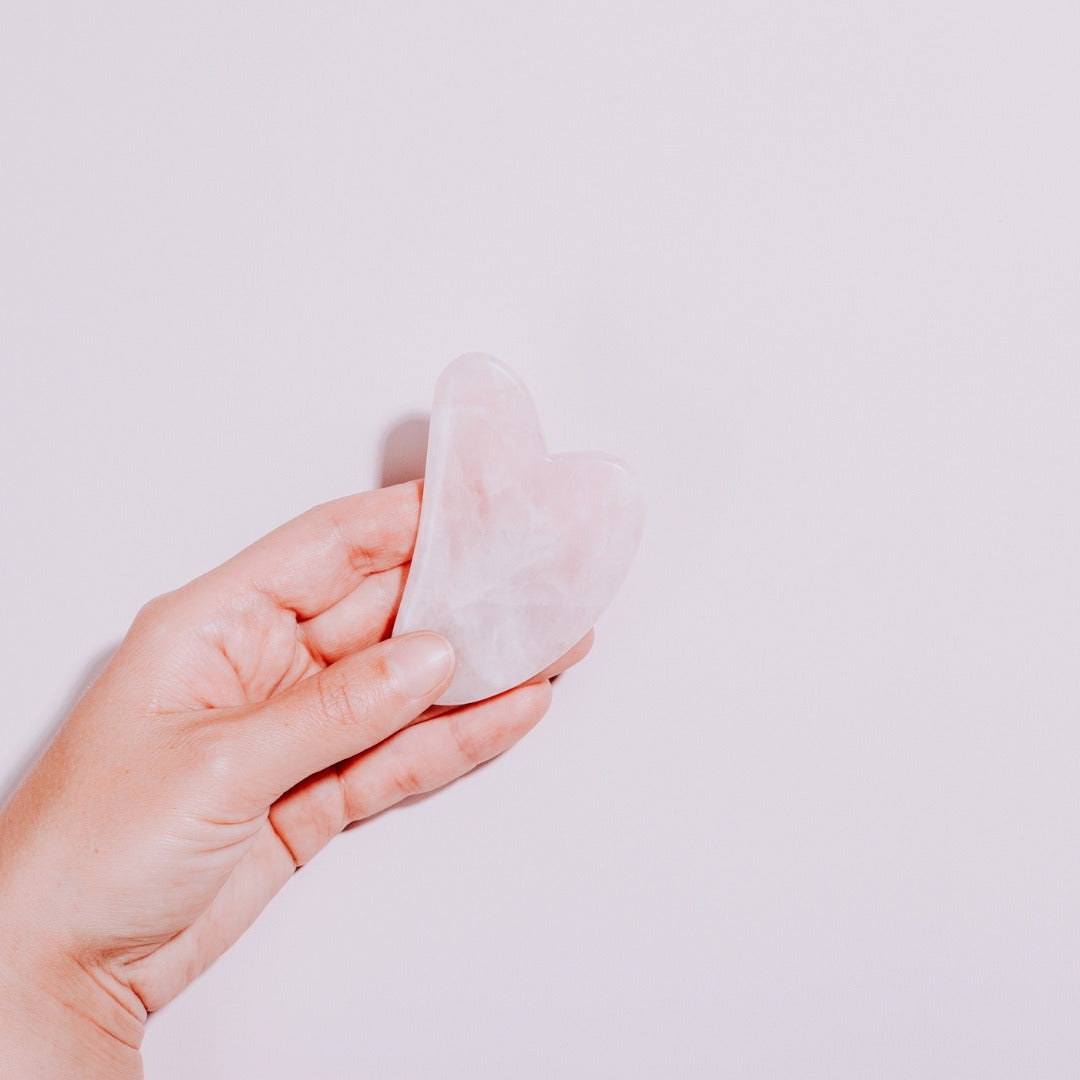 Gua Sha Cuarzo Rosada en una mano con fondo plano de Simple As.